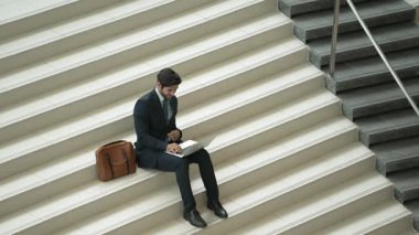 Merdivenlerde dizüstü bilgisayar kullanarak yatırımcıların çalışma ya da planlama stratejisinin en üst görüntüsü. Modern bir otelde dizüstü bilgisayar kullanarak veri analizi yapan takım elbiseli profesyonel bir iş adamı. Sevinçli..