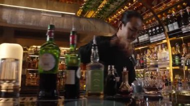 Asyalı barmen, kokteyl barında müşterilere ikram etmek için karıştırılmış bardağa buz küpü ve karışık kokteyl koyuyor. Hoş geldin içeceği ve etkileyici kostümlü profesyonellik ilk izlenimi. Vinosity.