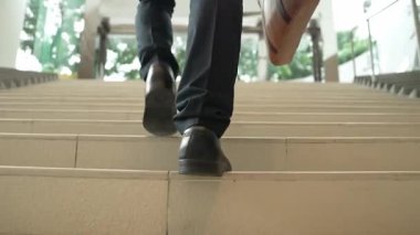 İş adamının bacağına yakın çekim merdivenleri çık. Başarılı bir adam merdivenleri çıkarken yeni bir şey keşfediyor. Seyahat etmek, terfi almak, yeni bir iş bulmak, yeteneğini artırmak. Arkadan bak. Sevinçli..