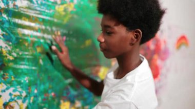 Mutlu Afrikalı çocuğun arkadan bakışı, resim dersinde günlük beyaz gömlek giyerken boyalı duvarı renkli eliyle boyadı. Mart öğrencisi yaratıcı sanat çalışması yapmak için el izi kullanıyor. Eğitim. Öğretim