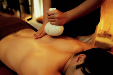 Sıcak bitkisel top spa masaj vücut tedavisi, masör erkek vücuduna nazikçe şifalı bitki torbası bastırıyor. Aromaterapi tesisinin sakinliği ve dinginliği kaplıca salonundaki mumların sıcacık ışığında. Sessiz.