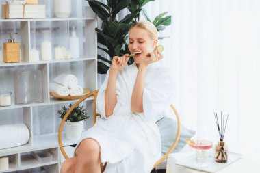 Elinde taze salatalık dilimleri tutan ve bornoz giyen bir kadın tatil köyünde ya da otelde lüks yüz derisi kaplıcalarının tadını çıkarıyor. Yüz ve güzellik tedavisi için cilt bakımı. Sessiz.