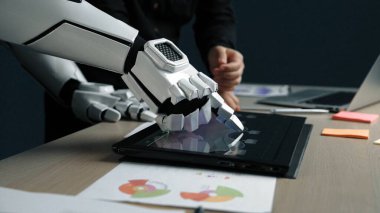 Robot bir el modern bir çalışma alanında dokunmatik ekranlı bir bilgisayarla temas kurar. İnsan varlığı veri analizi, sergilenen yenilikler konusunda işbirliği öneriyor.