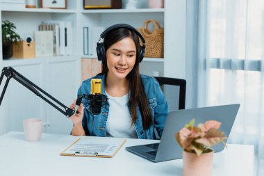 Sosyal medyada kulaklıkla canlı yayın yapan Asyalı sunucu modern stüdyoda yaşam koçluğu veya pazarlama dinleyicilerini selamlıyor. Taktik.