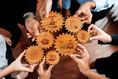 Bu resim, her biri vergi ve bütçe, takım çalışması ve stratejik planlama gibi çeşitli finansal kavramları temsil eden ahşap dişliler etrafında işbirliği yapan elleri resmediyor. Dostluk