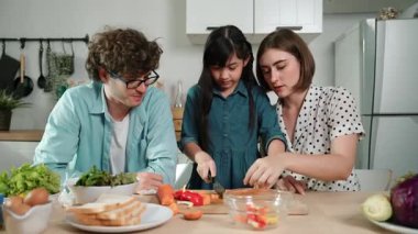 Çekici beyaz anne ve baba Asyalı kızıyla taze yemek pişirmek için birlikte vakit geçiriyorlar. Enerjik anne ve baba mutfakta salata yapmak için taze sebze hazırlıyor. Sağlıklı yiyecekler. Pedagoji.