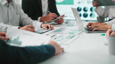 Bir grup iş adamı dinamik bir toplantıda yer alarak, bir belgede grafik ve çizelgeleri analiz ederek, modern bir çalışma alanında takım çalışması ve iletişimi sergilediler. SACTR