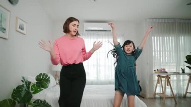 Yatak odasında Asyalı kızıyla müzik eşliğinde dans eden mutlu çekici anne. Beyaz anne dans eder ya da egzersiz yapar. Bu arada tatlı çocuk da müzik eşliğinde yatağa atlar. Aile eğlence konsepti. Pedagoji.