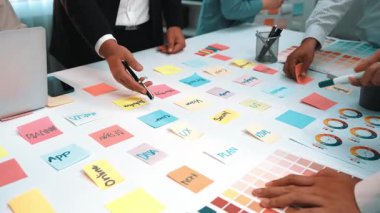 Çeşitli profesyonellerden oluşan bir grup, modern bir ofis ortamında fikirleri haritalamak ve düzene sokmak için yapışkan notlar kullanarak canlı bir beyin fırtınası yapıyor. SACTR