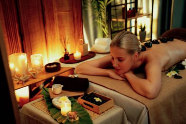 Lüks tatil köyündeki kaplıcalarda sıcak taş masajı, sıcak mum ışığı, spa bazalt taşı masajının keyfini çıkaran mutlu kadın müşteriler, rahatlatıcı bir sıcaklıkla vücudun üzerinde süzülüyorlar. Sessiz.