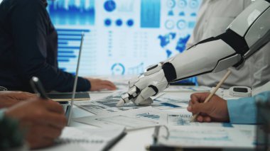 Robot bir elin finansal raporları ve grafikleri analiz ettiği, insanlar ve teknoloji arasındaki işbirliğini modern bir çalışma alanında sergilediği geleceksel bir iş toplantısı. Noogenesis