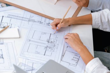 Asyalı kooperatif iş arkadaşı ev modelini ev modeliyle ve bina planıyla birlikte masaya koyarken, profesyonel güzel mimarın el yapımı taslaklarının en üst görüntüsü. Tertemiz..