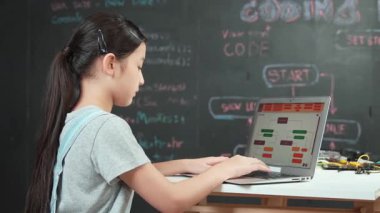 Genç mutlu Asyalı kız kodlama ve programlama tahtası başında. Lise öğrencisi, masada elektronik ekipmanlarla dizüstü bilgisayarı kullanarak mühendislik kodları yazıyor.