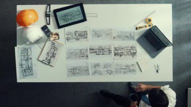Proje planını kontrol ederken ve seçerken mimar mühendisin bina planlarını masaya yerleştirdiği tepeden aşağı hava görüntüsü. İç mimar toplantı masasından mimari plan seçti. Hizalama.