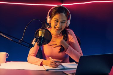 Geceleri podcast 'te olumlu konuşmalar yapan, pembe neon ışıklı modern stüdyoda sunum için dizüstü bilgisayar kullanan, gülümseyen, genç, güzel Asyalı bir etkileyiciydi. Taktik.