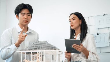 Güzel, genç, beyaz bir proje yöneticisi Asyalı mühendise, mühendislik masasında ev modelini ölçerken tablet kullanarak bina detaylarını anlattı. Tertemiz.