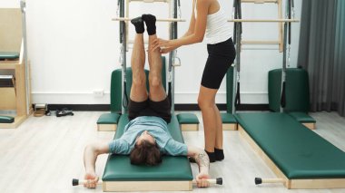 Pilates eğitmeni bir müşteriye paspasın üzerinde bacak esnetme sırasında rehberlik ediyor. İspanyol öğrenci, esnekliği ve çekirdek istikrarı artırmak için ters çatırtı ya da omuz duruşu yapıyor. Sağlık konsepti. Alışkanlık.