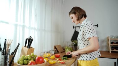 Enerjik anne, mutfak malzemeleri ile çevrili sebzeleri doğrarken modern mutfakta kahvaltı için salata yapıyor. Akıllı kadın temizlikçi yemek pişirir ve yemek hazırlar. Sağlıklı bir yaşam tarzı. Pedagoji.