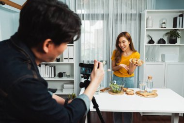Asyalı güzel kadın yemek uzmanı akıllı kameramanların sosyal medyada canlı yayın yaptığı canlı kanal kamerasında sağlıklı tahıllı çörek sepeti sunuyor. İnfobahn.