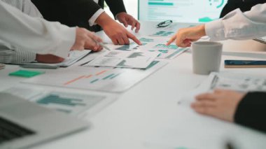 Dinamik bir iş ekibi, işbirlikçi bir toplantı sırasında finansal veri analizi yapar. Masada çeşitli grafik ve belgeler gösterilerek takım çalışması ve stratejisi vurgulanıyor. SACTR