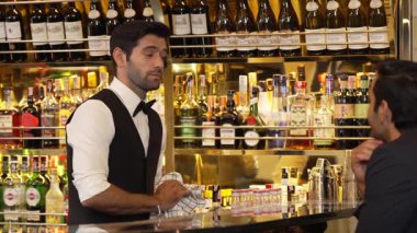 Güzel görünümlü barmen, VIP müşterisiyle içki tezgahında samimi, güler yüzlü bir şekilde sohbet ederken çekici bir profesyonellikle karşılama içkisi sunuyor ve harika bir ilk izlenim bırakıyor. Vinosity.