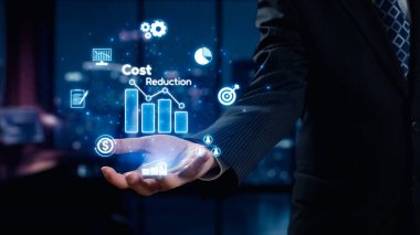 Bir işadamı, dijital grafikler ve sembollerle vurgulanan ileri maliyet düşüşü kavramlarını sergiliyor ve gece çağdaş bir ofis ortamındaki yenilikleri vurguluyor. Dörtgen