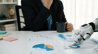 Bir iş adamı, elinde kahve fincanı tutarken grafiklere işaret eden bir robot eliyle analiz yaparak teknolojinin modern çalışma alanlarına entegrasyonunu gösteriyor. Noogenesis