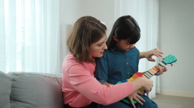 Kafkasyalı bir anne evde akustik müzik öğretirken ukulele çalan mutlu kız. Sevimli çocuk enstrüman öğreniyor. Kafkasyalı mutlu anne ve kız birlikte vakit geçiriyorlar. Pedagoji.