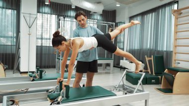 Bir pilates eğitmeni, müşteriye bir ıslah makinesinin tahta varyasyonunda rehberlik eder. Sağlıklı bir kadın, dengeyi geliştirmek için antrenör yardımı ile yenilikçi üzerinde yan kalas değişimi yapıyor. Alışkanlık.