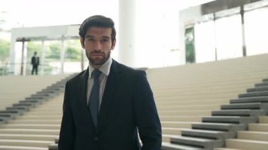 Akıllı iş adamı merdivenlerde kameraya bakıyor. İş elbisesi giyerken kameraya gülümseyen başarılı adamın yakın çekimi. Yönetici, kameraya bak. Hareket eden kamera. Sevinçli..