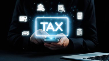 Parlak vergi sembolleri ve finansal planlama ve yönetim simgelerini gösteren bir akıllı telefon kullanan bir kişi. Karanlık arka plan dijital odağı arttırır. Dörtgen