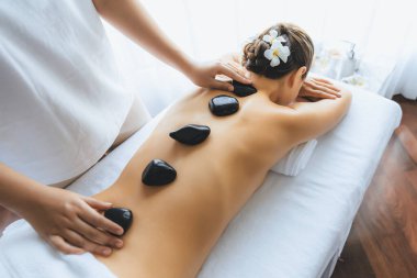 Lüks tatil köyündeki kaplıcalarda sıcak taş masajı. Gün ışığı sükunet ortamında, mutlu kadın müşteri bazalt taş masajından zevk alıyor. Rahatlatıcı bir sıcaklıkla vücudun üzerinde süzülüyor. Sessiz.