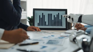 Profesyonellerin ekrandaki verileri analiz ettiği modern bir iş toplantısı. Etkinlikte teknoloji ve işbirliği, sergilenen tablolar ve tartışmalar üzerinde duruluyor. Noogenesis