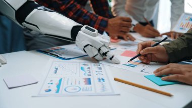 Bir strateji toplantısı sırasında veri tabloları ve grafiklerini analiz eden robot kol ve insan elleri arasındaki işbirliğini gösteren dinamik bir çalışma alanı. Noogenesis