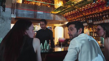 Asyalı barmen alkollü likör ve şerbetli kokteyl bardağıyla süslenmiş noel ağaçlarında gece kulübündeki VIP çiftlere taze içecek servisi yapıyor. Vinosity.