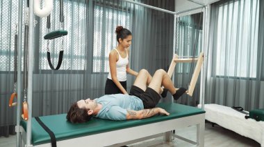 Cadillac ekipmanları üzerinde bacak kaldırma egzersizinde müşteriye yardımcı olan yetenekli pilates eğitmeni. Kadın antrenör, Cadillac 'ın bacak gerdirme hareketine yardım ediyor. Temel bağlantıyı geliştirmek için, bacak esnekliği için. Alışkanlık.