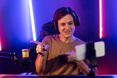 Oyun kanalı, online oyun oynayan akıllı flamalı oyun sunucusu, kulaklık takan, neon ışıklandırma odasındaki takım oyuncusuyla akıllı telefondan canlı yayında konuşan izleyiciler. Bireysel.