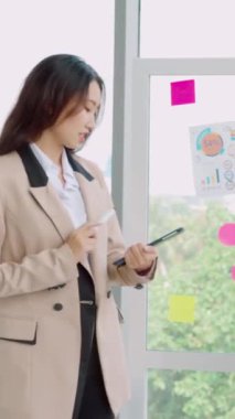 İş adamları ofisteki proje planlama kurulunda çalışıyor ve proje gelişimini analiz etmek için iş arkadaşlarıyla sohbet ediyorlar. Düzenli olması için cam duvara yapıştırılmış yapışkan notlar kullanıyorlar. .