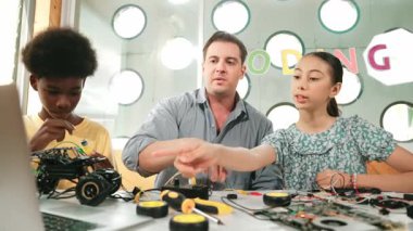 Kafkas öğrenci, öğretmene şifreyi soruyor ve bilgisayar ekranını işaret ediyor. Profesyonel eğitmen kız sorusuna cevap verirken, erkek çocuk da elektronik aletli araba modelini tamir ediyor. Öğretim