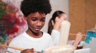 Akıllı Afrikalı çocuk tuvali boyarken, tatlı kız da arkadan çiziyor. Sanat dersinde. Lise öğrencisi renkli duvarların önünde durarak yaratıcılık fikri ile sanat eserleri yaratıyor. Öğretim