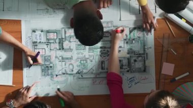 İnşaat mühendisi ekibinin renkli paletlerle toplantı masasında yazı yazması. Yönetici proje planlarına bakarken bir grup farklı insan plan yapıyor ve not alıyor. Sempozyum.