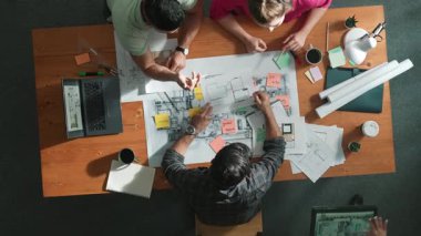 İnşaat mühendislerinin masa başında proje planıyla otururken tablet kullanarak ev yapısını dizayn etmelerine tepeden aşağı bir bakış açısı. Ekip planlama ve inşaat hakkındaki fikirlerin havadan görüşü. Sempozyum.