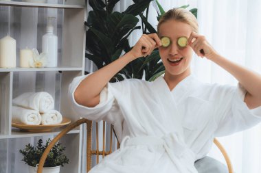 Elinde taze salatalık dilimleri tutan ve bornoz giyen bir kadın tatil köyünde ya da otelde lüks yüz derisi kaplıcalarının tadını çıkarıyor. Yüz ve güzellik tedavisi için cilt bakımı. Sessiz.