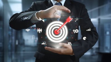 Bir iş adamı, başarı ve stratejiyi simgeleyen parıldayan bir hedef grafiğine odaklanır. Bu görüntü yeniliğin ve teknolojinin özünü modern bir çalışma ortamında yakalar. Dörtgen