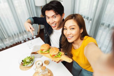 Gülümseyen ev sahibi aşçıların akıllı telefonuyla fotoğraf çekerken üst görüntüsü yemek programında çift hamburger tutarken sosyal medya kanalında ev yapımı salata tabağıyla kolaylıkla görülebiliyor. İnfobahn.