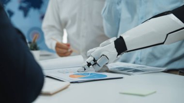 Robotik bir el modern bir ofiste yapılan ortak bir toplantıda teknolojinin kurumsal stratejiler ve analizlere entegrasyonunu gösteren bir iş grafiğine işaret eder.