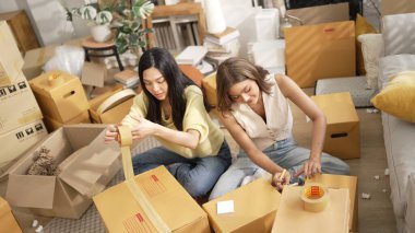 Çekici bir oda arkadaşı oturma odasında paket paketlerken pakette konum yazıyor. Mutlu satıcı birlikte çalışıyor ve teslimat paketini hazırlıyor. Girişimci kargo kutusu paketliyor. Myrmidon.