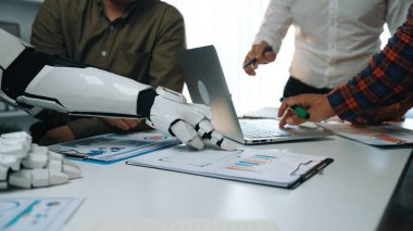 Bir insan ve robot el ofis ortamında birlikte çalışır, teknoloji ve görsel verilerle etkileşim içinde, iş dünyasındaki işbirliğini ve yeniliği sembolize eder.