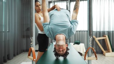 Eğitmen rehberliğinde Pilates Cadillac 'ta ters bacak yükseltme pratiği yapan sağlıklı bir müşteri. Çekirdek dayanıklılığını ve üst vücut dengesini arttırmak için Cadillac 'ı geren adam. Alışkanlık.