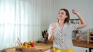 Enerjik beyaz anne kahvaltı için salata pişirirken ve yemek pişirirken elinde kepçeyle şarkı söylüyor. Sağlıklı yemek yapmaya hazırlanırken müziğe yönelen mutlu ev sahibi. Pedagoji.